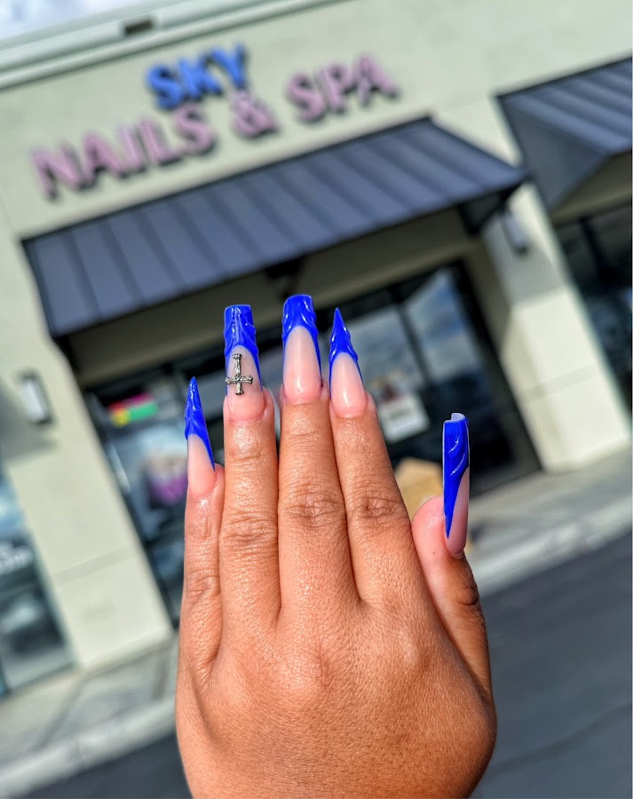 Deep-blue chrome nails held up in front of the Sky Nails & Spa storefront sign in Cathedral City